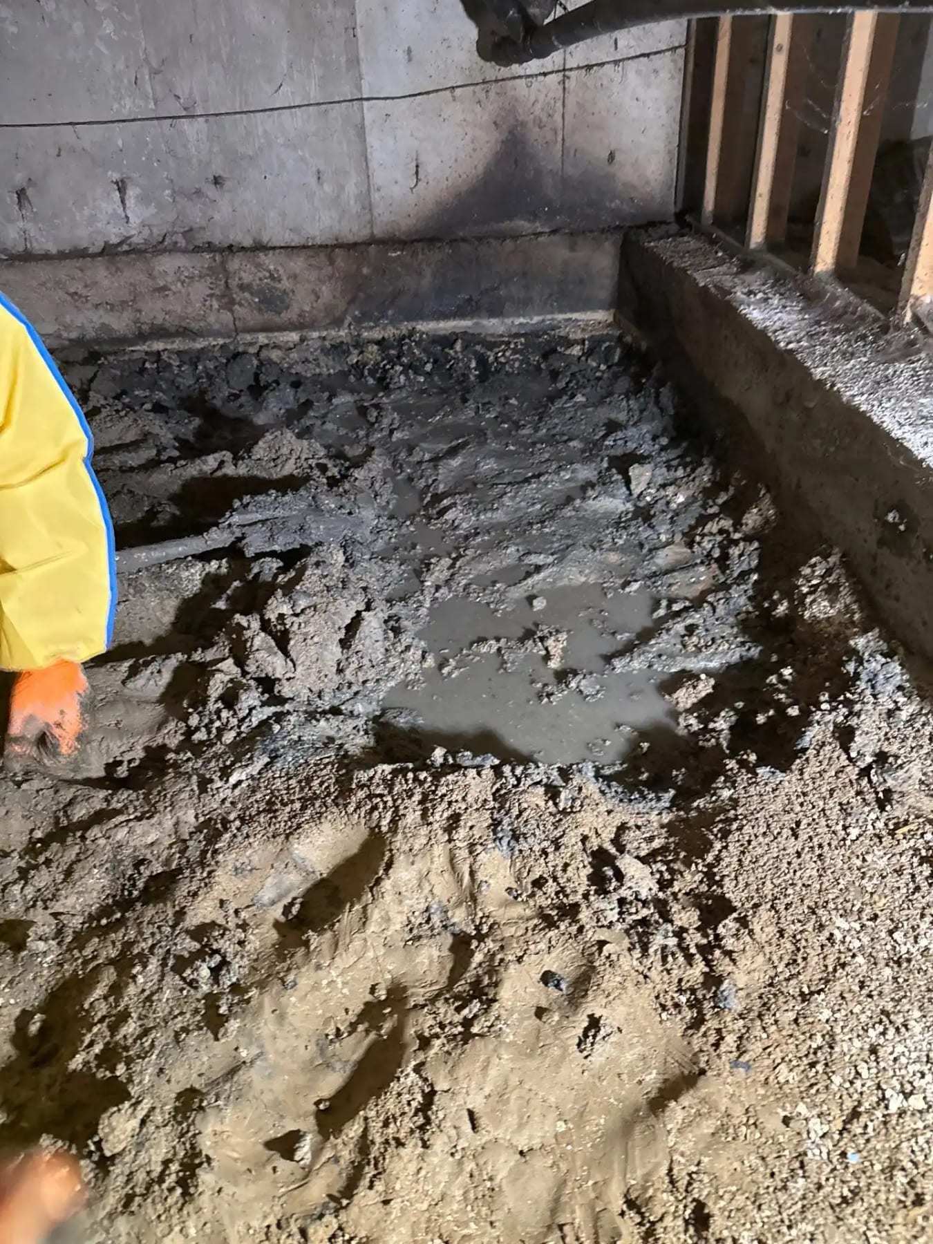 Mud and sewage residue on a floor beside a worker in a yellow suit